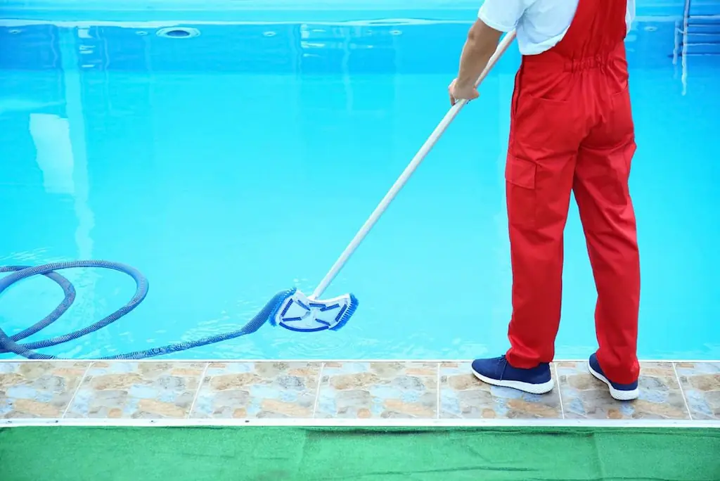 Pool service company worker cleaning with brush